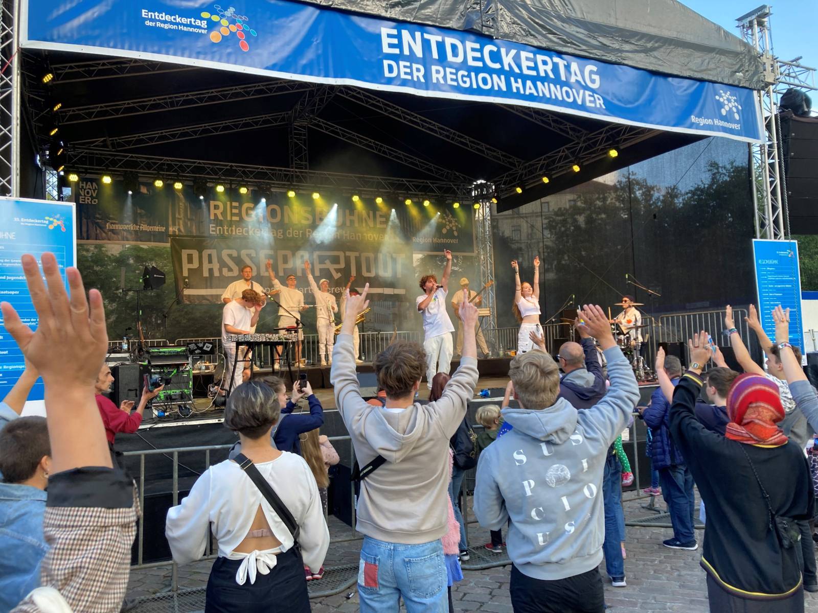 Eine junge Musikgruppe auf einer Bühne, davor heben Menschen ihre Hände in die Höhe